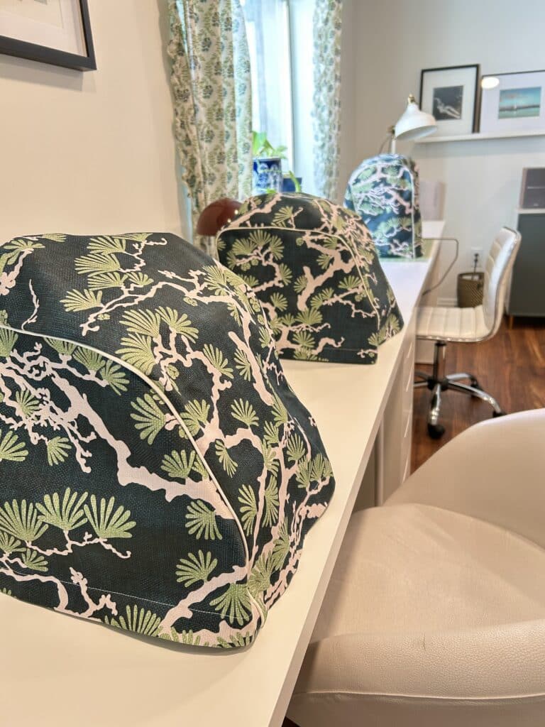 Three covered sewing machines in a row on a long table. 