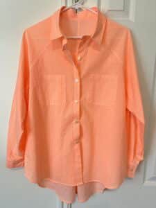 a neon peach mini-striped shirt hangs in front of a white door