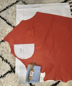 A coral leather hide and bag pattern pieces and hardware on a white fluffy rug