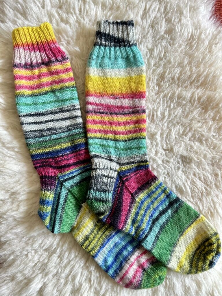 A pair of rainbow stripe socks on a fulffy white sheepskin 