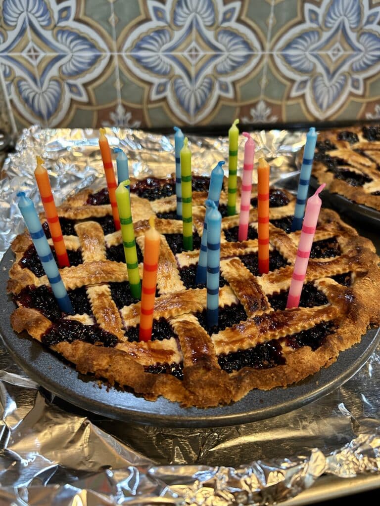 A slightly burnt blueberry pie with colorful candles in it 