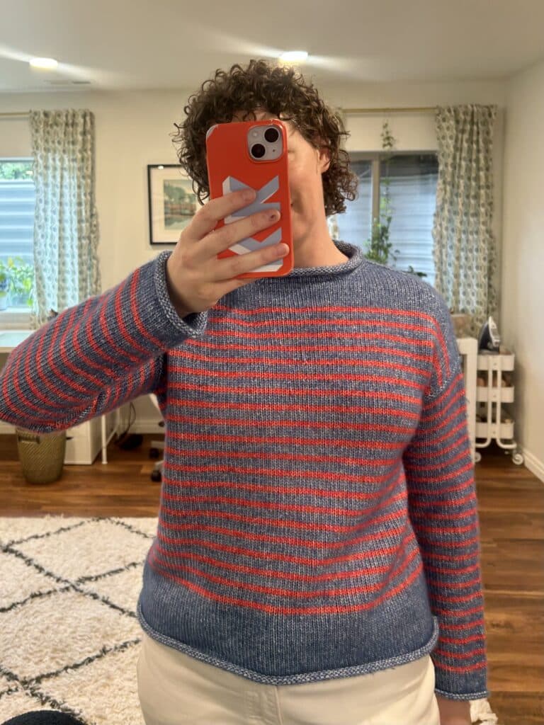 A woman taking a mirror selfie. She's in a blue sweater with red stripes.