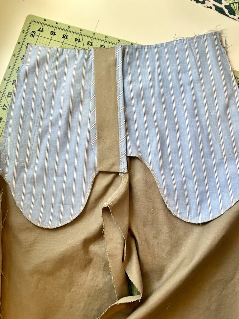 A pair of tan pants being sewn, with the inside front pockets showing. The pockets are blue striped cotton.