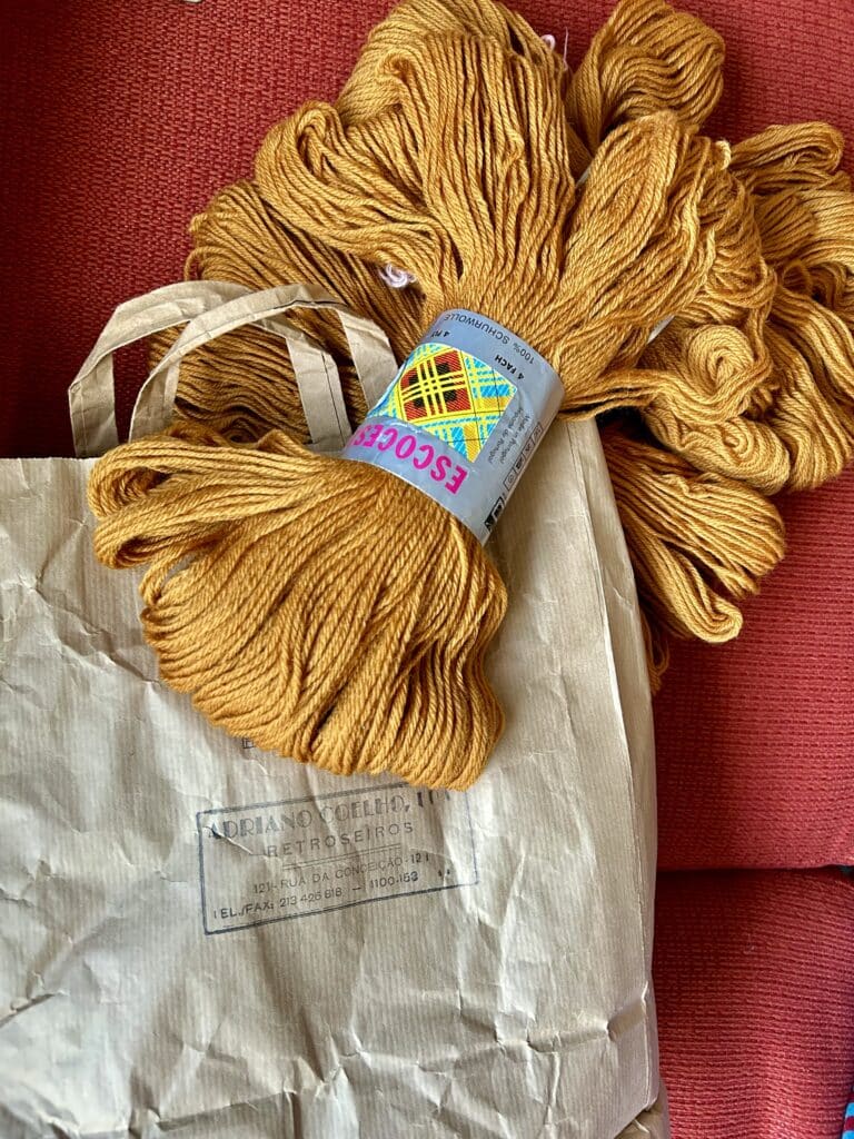 Skeins of unwound ochre-colored yarn spilling out of a brown shopping bag with a Portuguese store logo 