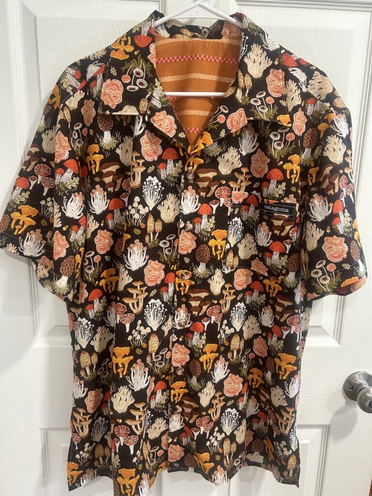 A men's shirt on a hanger, in a print of orange and white mushrooms on a brown background.