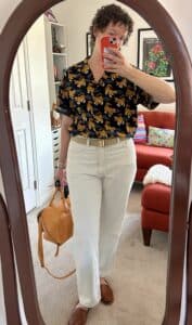 A woman takes a mirror selfie. She's wearing the tiger shirt, classic cut light blue jeans, a military belt, and woven shoes.