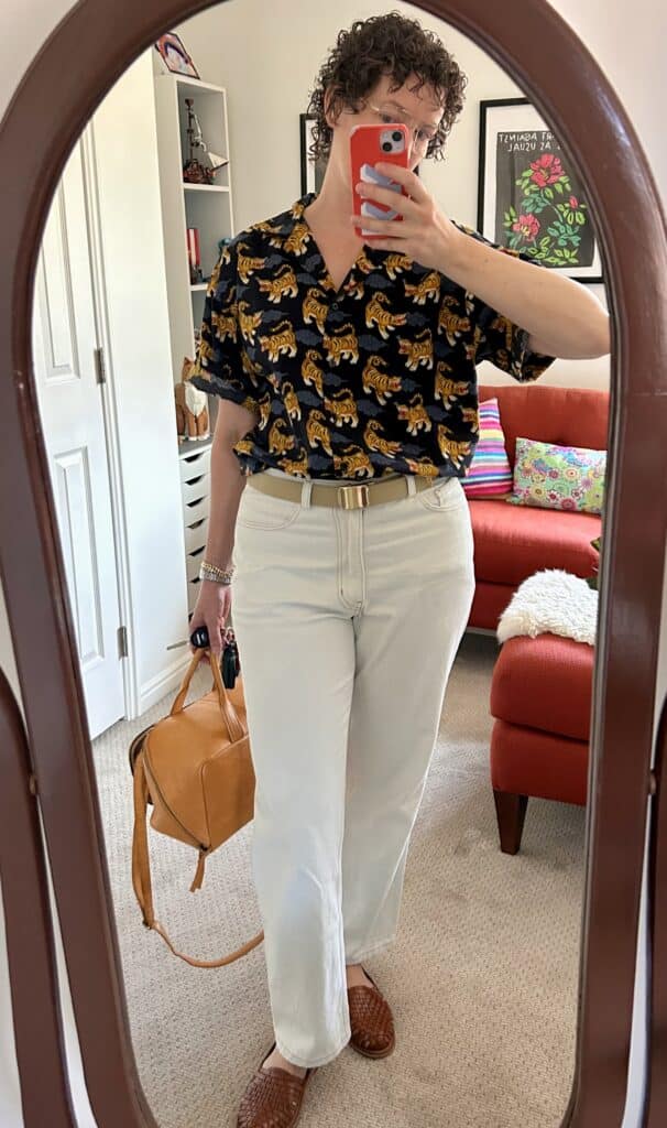 A woman takes a mirror selfie. She's wearing the tiger shirt, classic cut light blue jeans, a military belt, and woven shoes.