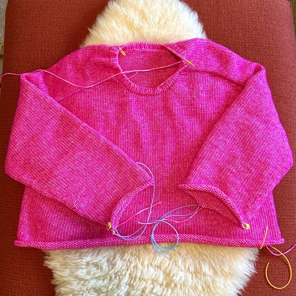 A sweater being knit in shocking pink yarn. It's about three-quarters done.