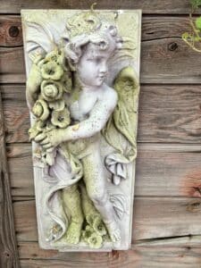A mossy decorative plaque of a cherub on the side of a wood shed