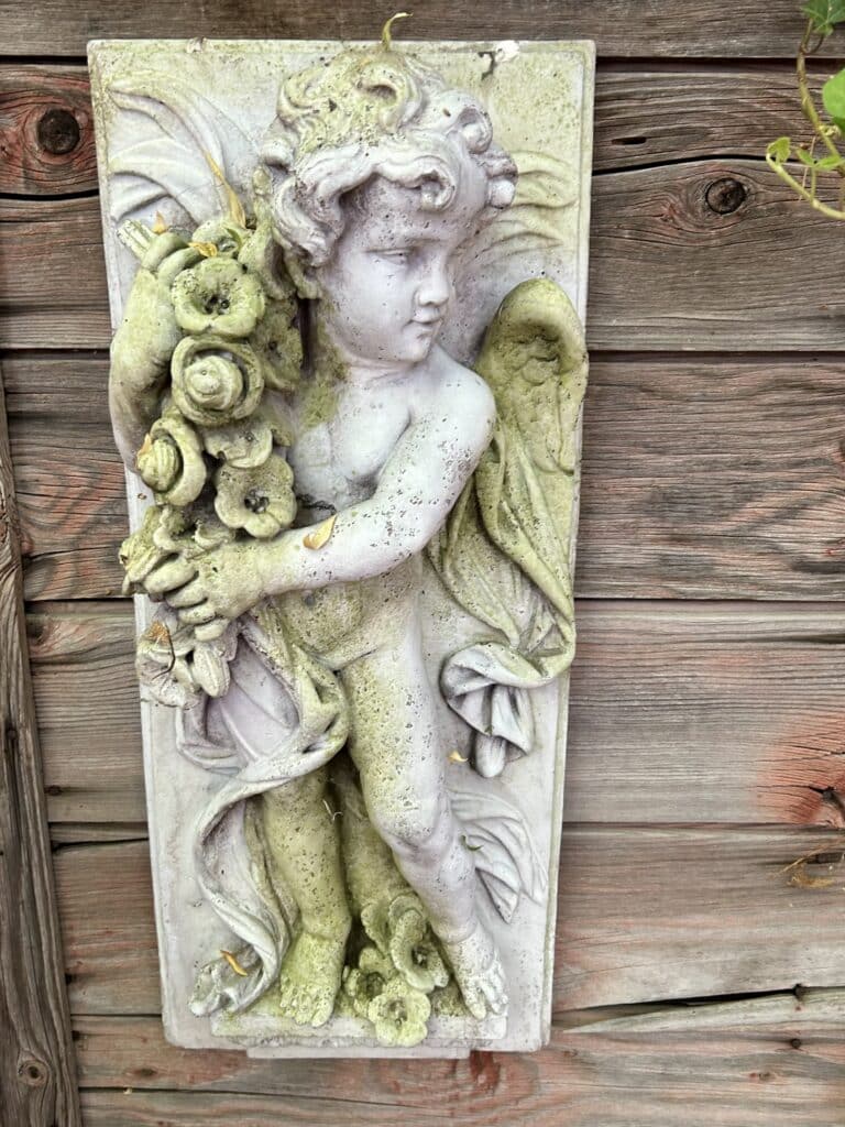 A mossy decorative plaque of a cherub on the side of a wood shed