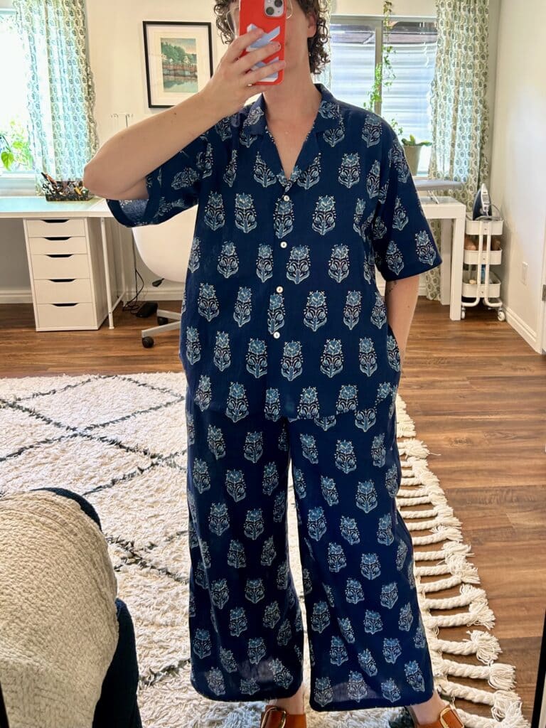 A woman's full-length mirror selfie. She's wearing a matching short sleeve button-up shirt and wide pants in a navy blue block print with light blue geometric floral motifs.