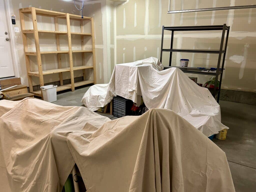 A garage interior with raw drywall and piles of stuff covered by drop cloths