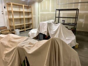 A garage interior with raw drywall and piles of stuff covered by drop cloths