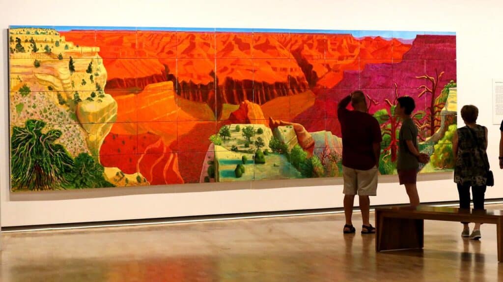 David Hockney's "A Bigger Grand Canyon" hanging in a museum, with a group of visitors.