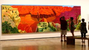David Hockney's "A Bigger Grand Canyon" hanging in a museum, with a group of visitors.