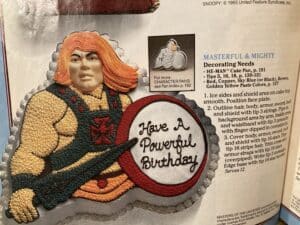 Page from the Wilton book showing a He-Man cake with a shield that says, Have a Powerful Birthday