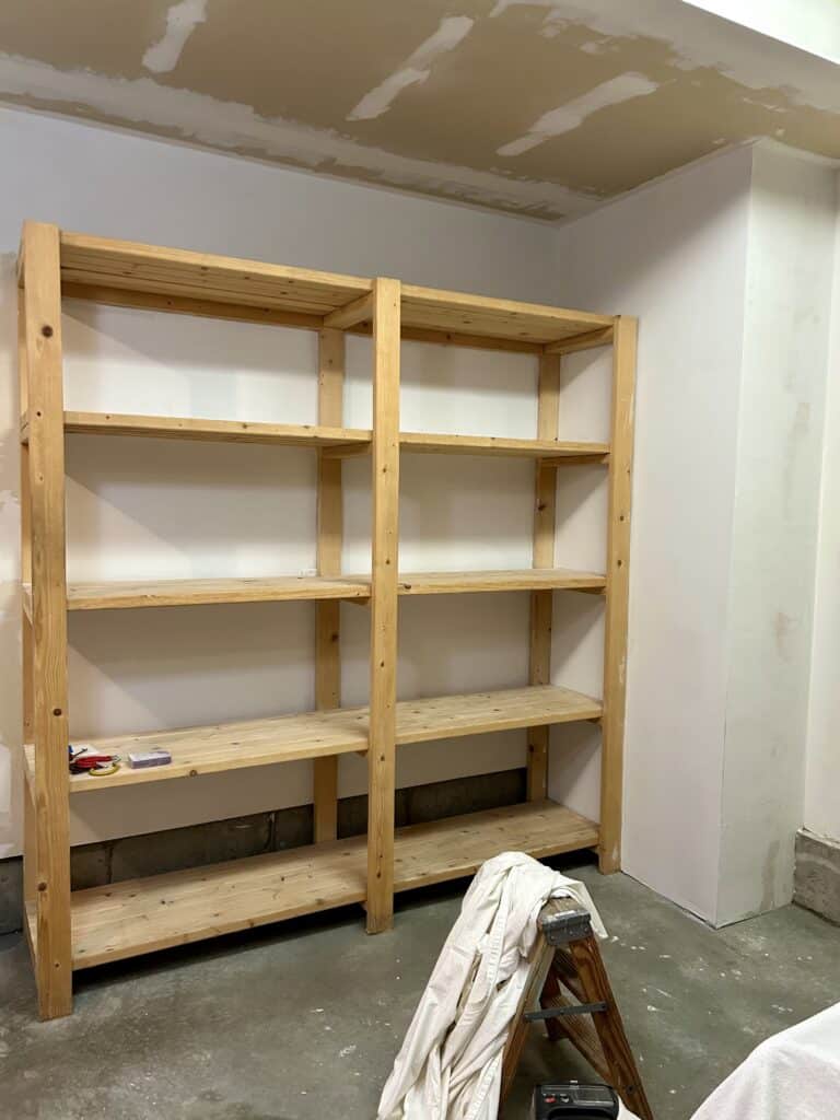 A built in shelf in a corner of a garage. The walls are covered with primer. 