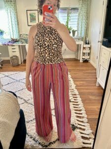 A woman wearing rainbow striped pants and a leopard top takes a selfie in a mirror