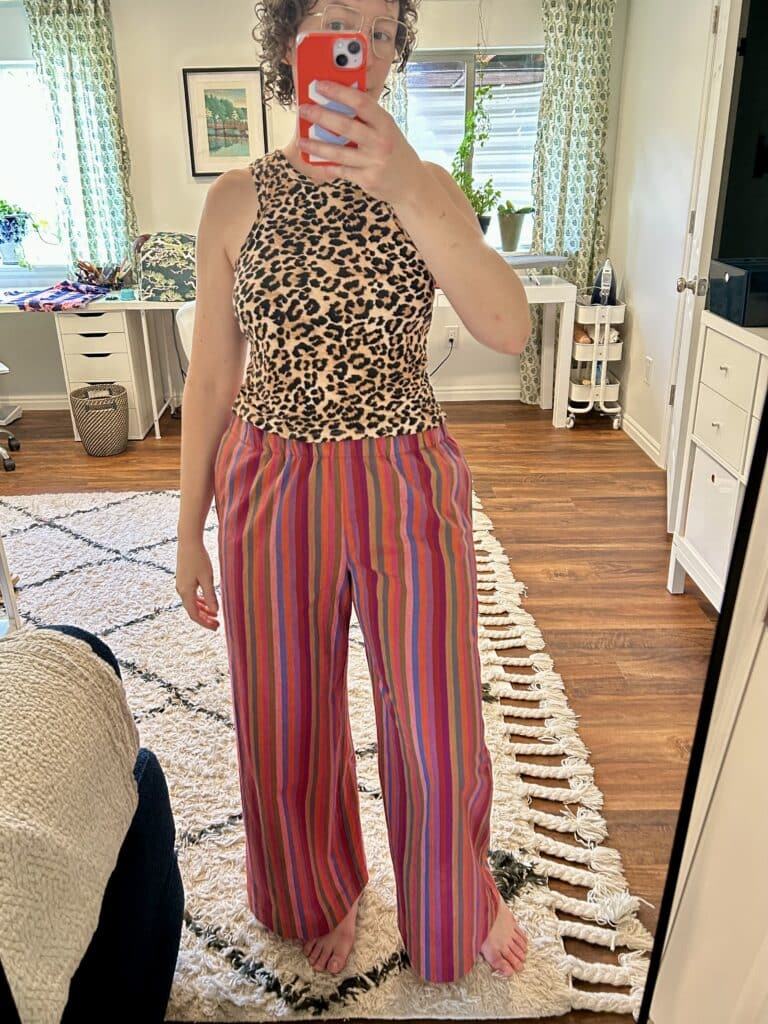 A woman wearing rainbow striped pants and a leopard top takes a selfie in a mirror 