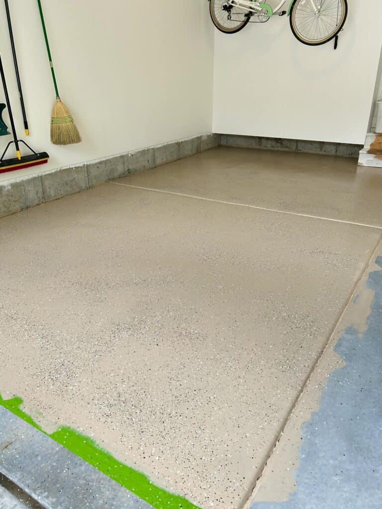 A half-painted garage floor. The left side is covered in tan epoxy, the right side is bare concrete.