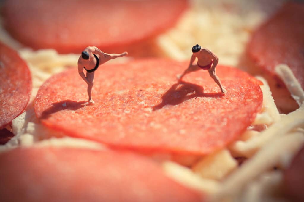 A photo by David Gilliver showing tiny sumo wrestlers squaring off on a pepperoni on an unbaked pizza
