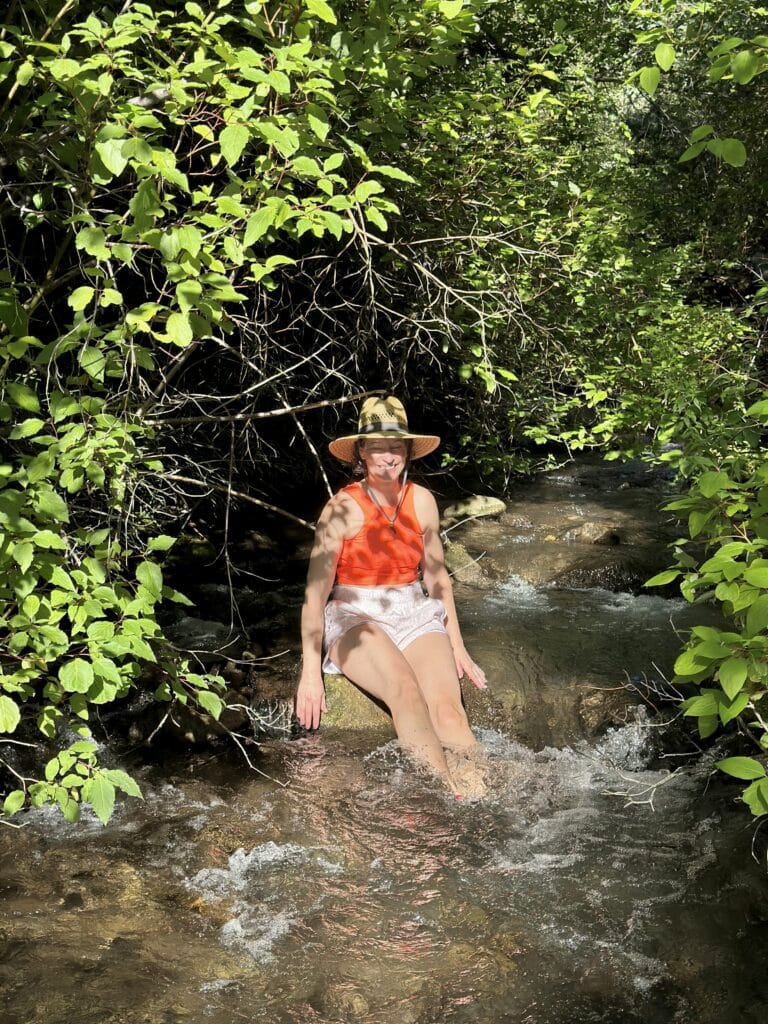 a woman in a big hat sitting on a rock in a mountain stream