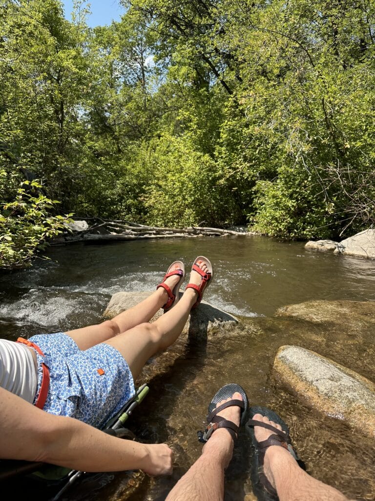 The legs and feet of a man and a woman propped up on rocks in a stream