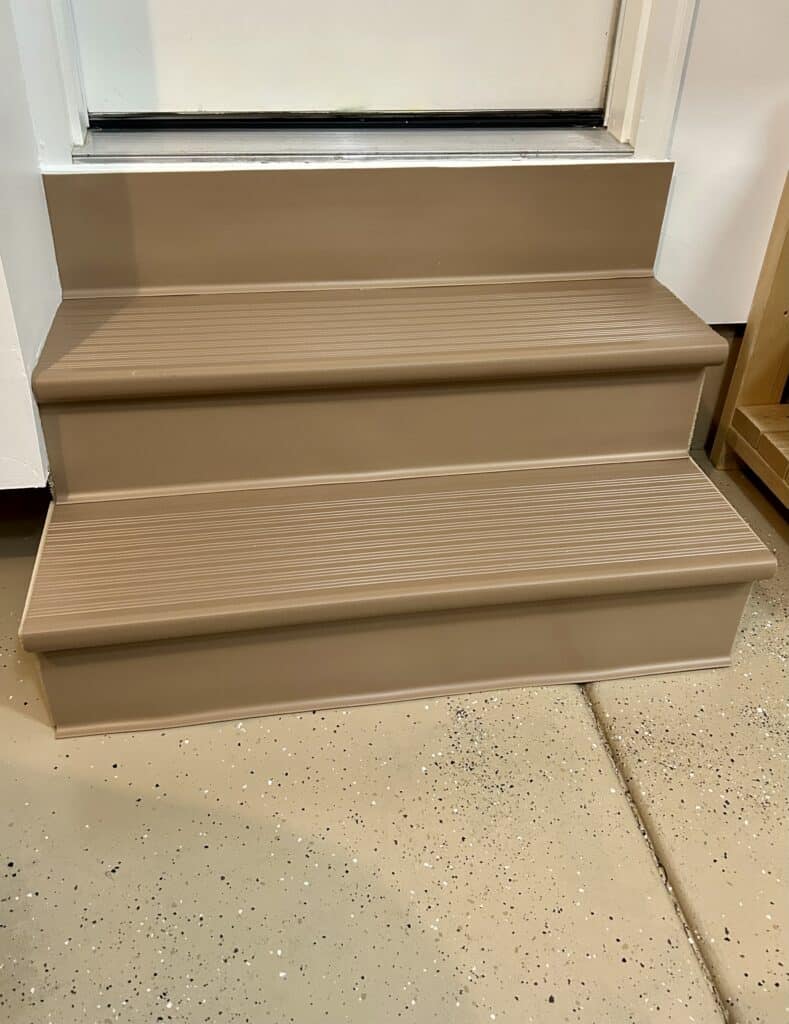 Two shallow stairs from the garage to the house door. They are covered in beige vinyl commerical treads and risers.