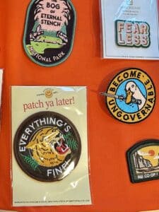 A few patches on orange fabric. One includes a roaring tiger with EVERYTHING'S FINE and another has a duck holding a knife with the words BECOME UNGOVERNABLE