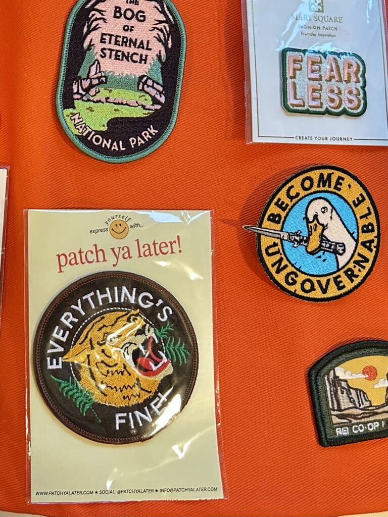 A few patches on orange fabric. One includes a roaring tiger with EVERYTHING'S FINE and another has a duck holding a knife with the words BECOME UNGOVERNABLE