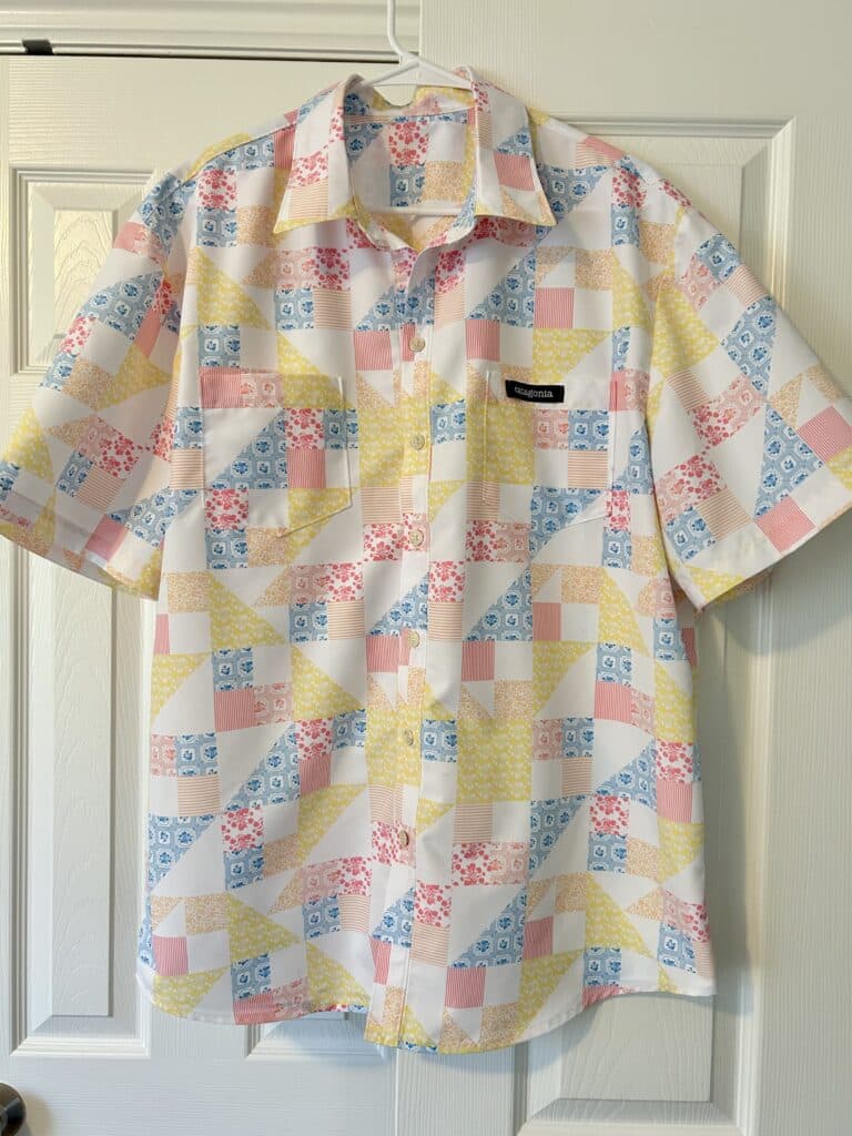 A men's shirt hangs on a closet door. It has a pink, yellow and blue quilt print on a white background.